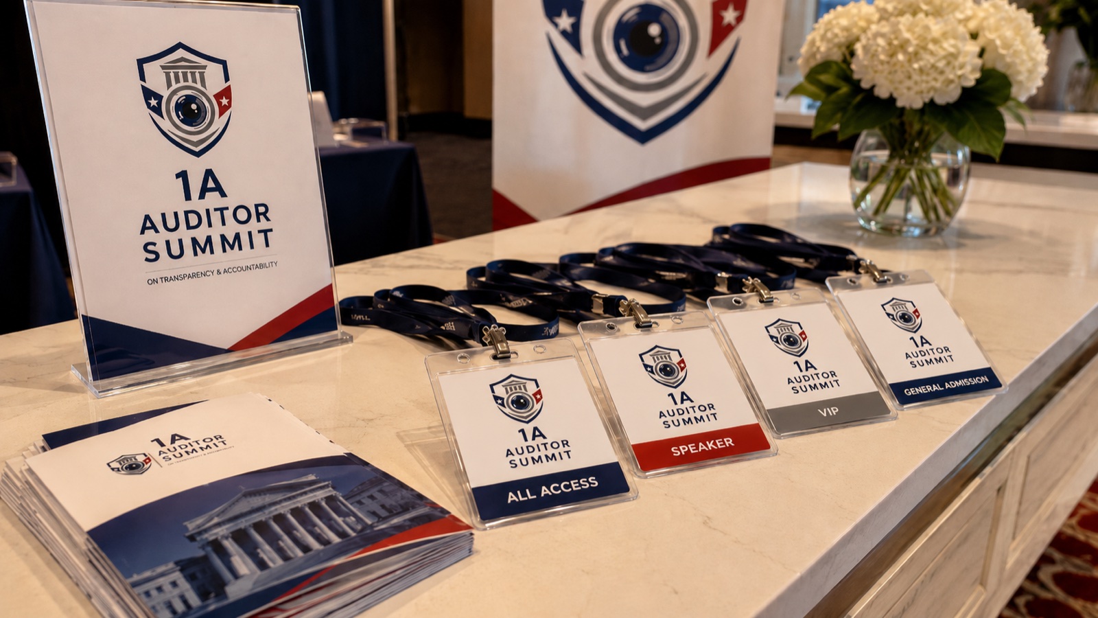 1A Auditor Summit branded badges on the check-in table — All Access, Speaker, VIP, and General Admission lanyards beside printed materials